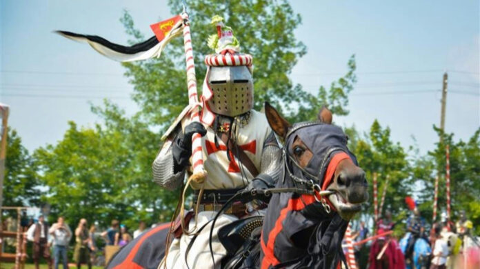 A rider in armour with a spear on a horse. The action takes place at a medieval festival.